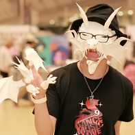 A paper artist wearing two of his creations - a demon mask and a dragon hand puppet.