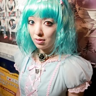 A Japanese girl in a doll's dress with turquoise hair and colored contact lenses.