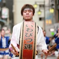 A man carrying a big Japanese drum in front of his dance group.