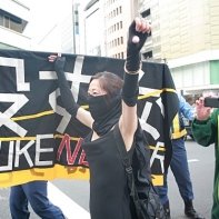 A masked woman protesting next to a banner at the 'Stop Nuclear Power' demo in Shinjuku.