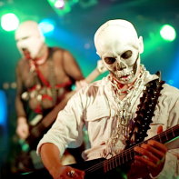 Multico in his psycho skeleton outfit playing his instrument with Hirohisa Nagao behind him.